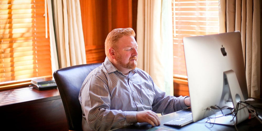 A man sitting behind desk working on a computer.