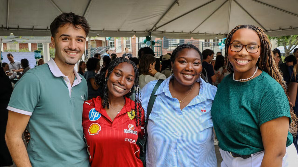 Four smiling diverse young adults pose at an outdoor event.