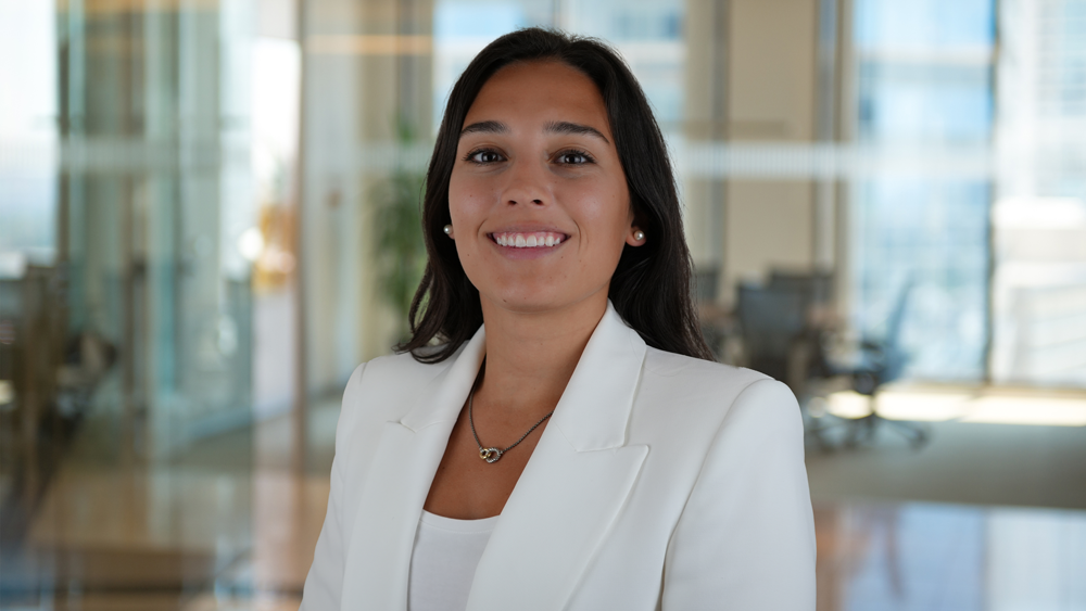 Smiling woman in white blazer against a modern office background.