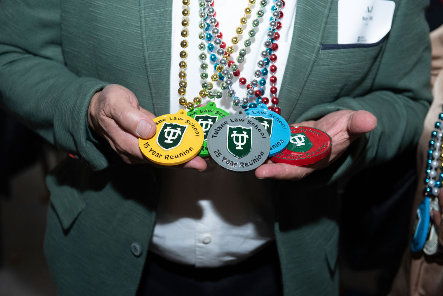 Hands holding four colorful medallions with a university logo, on beaded necklaces.