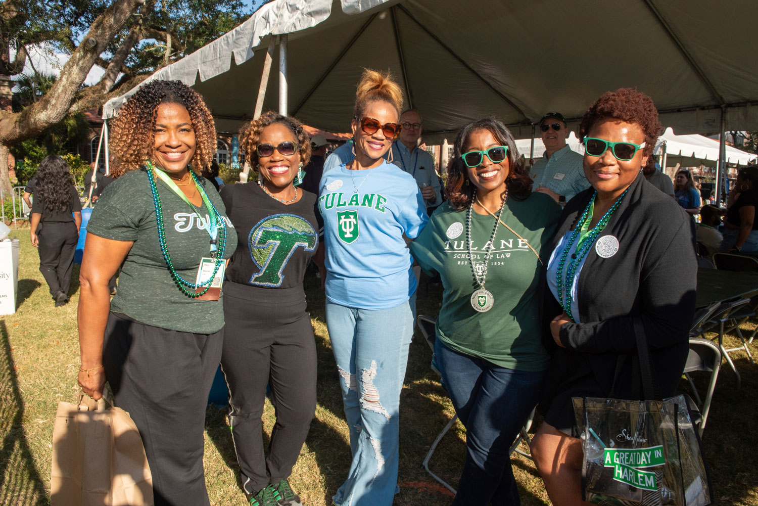 Five smiling women in Tulane shirts pose together at an outdoor event.