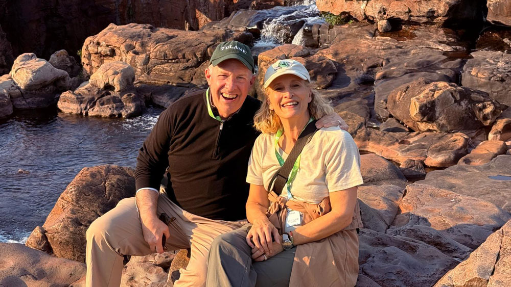 Ginny Wise and Kevin Wilkins smiling on red rocks, waterfall in background.