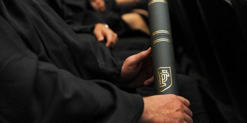 Black robed graduates holding rolled up degree.