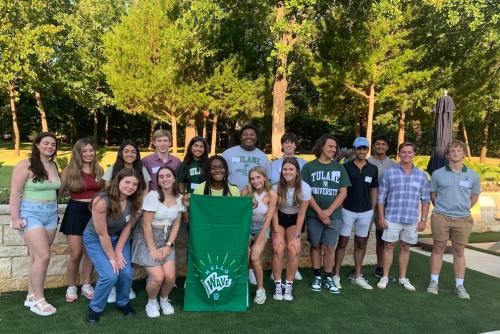 Incoming students in a park posing with Green Wave flag.